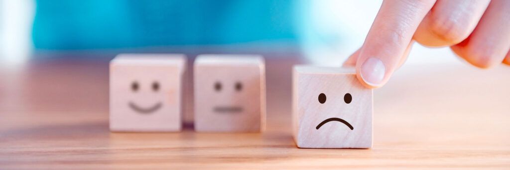 Cubos com rostos tristes simbolizando emoções, saúde mental e bem-estar emocional.