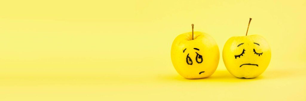 Duas maçãs com expressões de tristeza feitas a caneta.