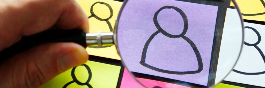 Lupa destacando ícone de pessoa em post-it simbolizando recrutamento e gestão